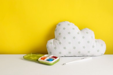 Cloud shaped pillow, thermometer and container with pillows on color background