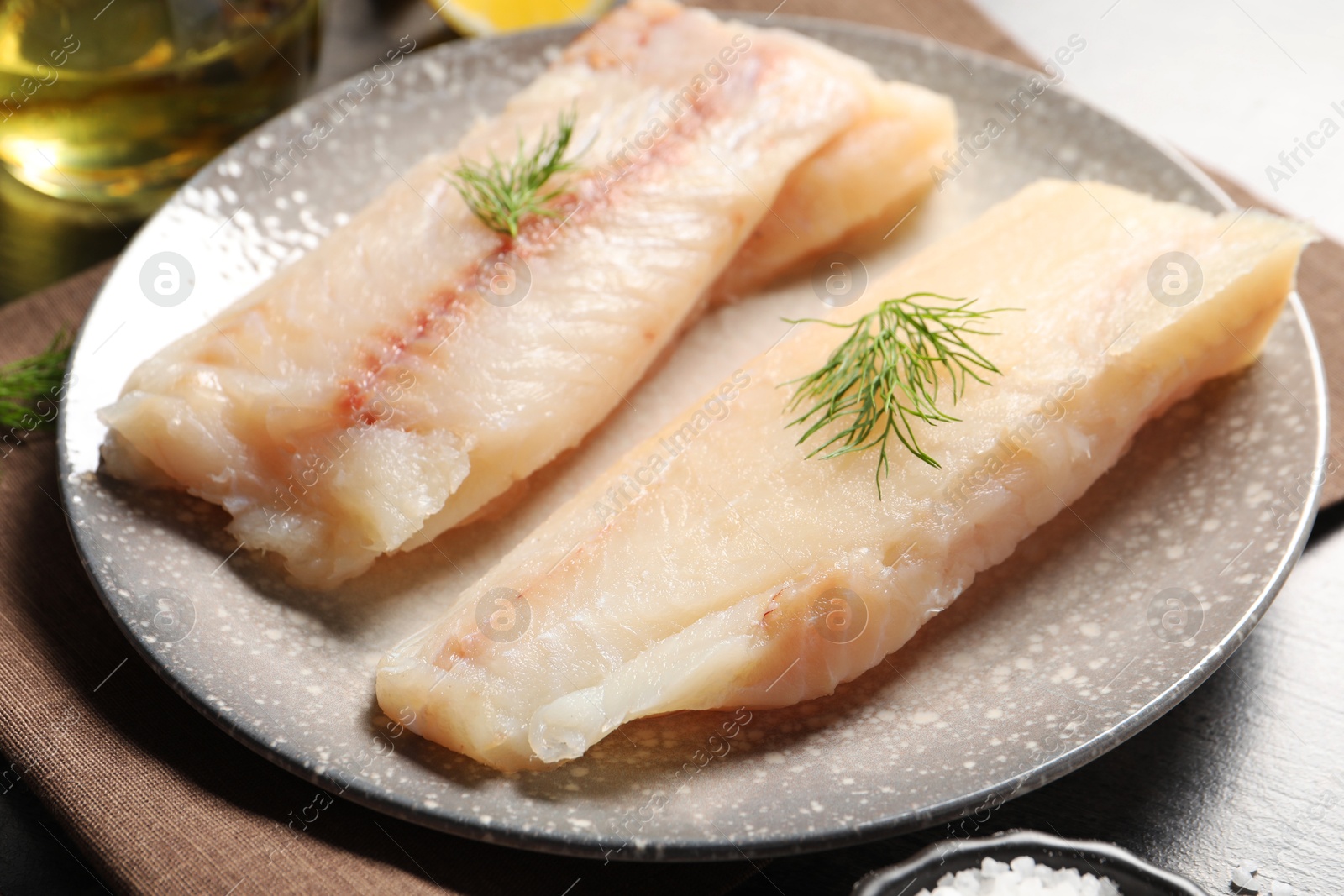 Photo of Pieces of raw cod fish and dill on table, closeup