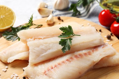 Photo of Pieces of raw cod fish, spices and parsley on table, closeup