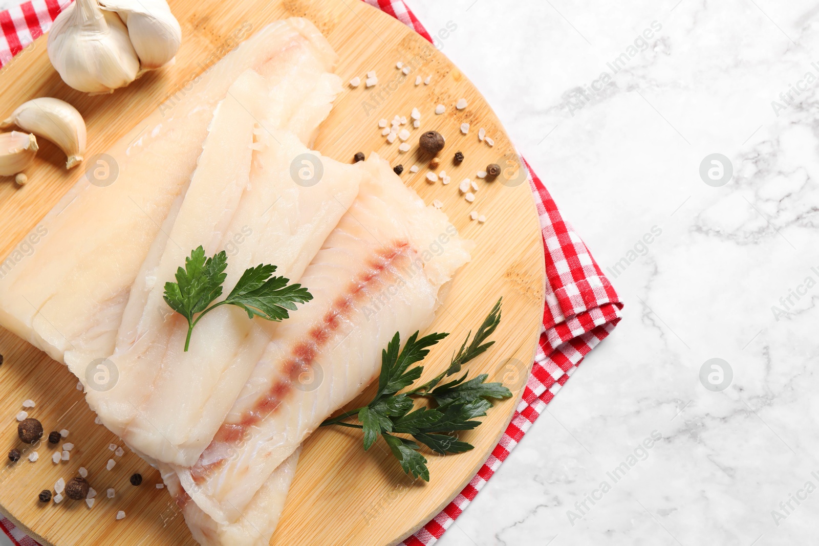 Photo of Pieces of raw cod fish, spices, garlic and parsley on white marble table, top view. Space for text