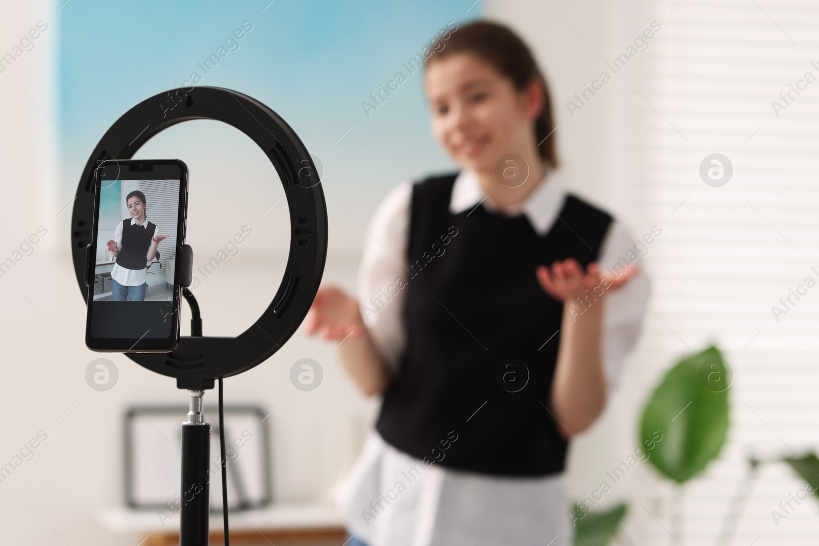 Photo of Teenage blogger explaining something while streaming at home, focus on smartphone