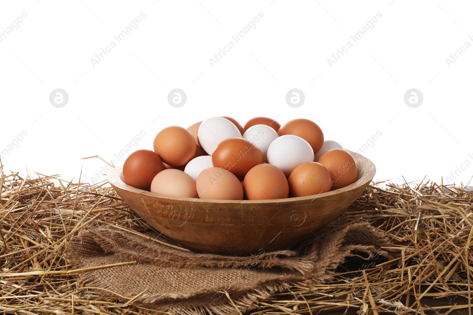 Photo of Fresh chicken eggs in bowl and dried straw on table against white background