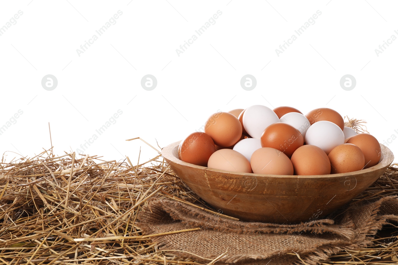 Photo of Fresh chicken eggs in bowl and dried straw on table against white background
