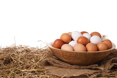 Photo of Fresh chicken eggs in bowl and dried straw on table against white background