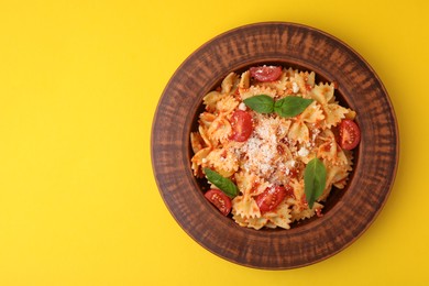 Tasty pasta with tomato, cheese and basil on yellow table, top view. Space for text