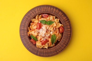 Tasty pasta with tomato, cheese and basil on yellow table, top view