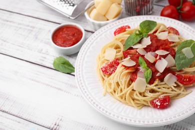 Tasty pasta with tomato sauce, cheese and basil on white wooden table, space for text