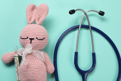 Toy bunny, stethoscope and thermometer on turquoise background, flat lay