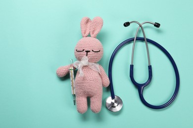 Photo of Toy bunny, stethoscope and thermometer on turquoise background, flat lay. Space for text