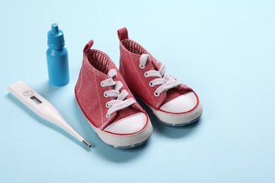 Photo of Kid's sneakers, thermometer and nasal spray on light blue background
