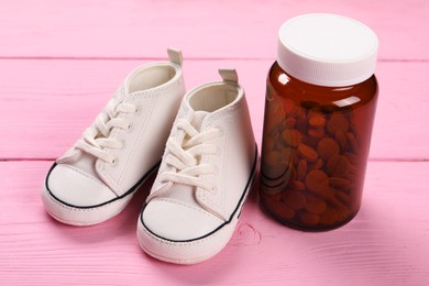 Photo of Kid's sneakers and pills on pink wooden background, closeup