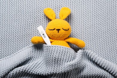 Photo of Toy bunny with thermometer under blanket, top view