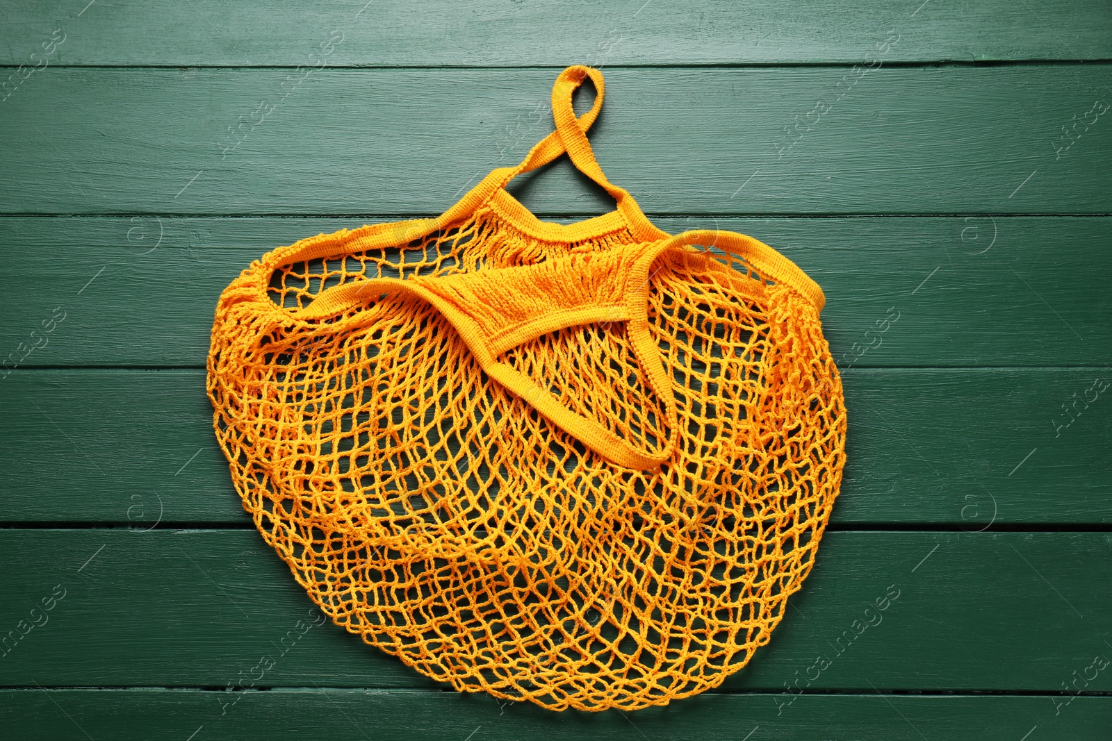 Photo of Orange string bag on green wooden table, top view