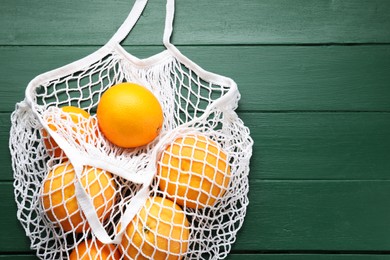 Photo of String bag with oranges on green wooden table, top view. Space for text