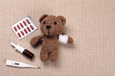 Photo of Toy bear with bandage, thermometer, pills and nasal spray on blanket, flat lay. Space for text
