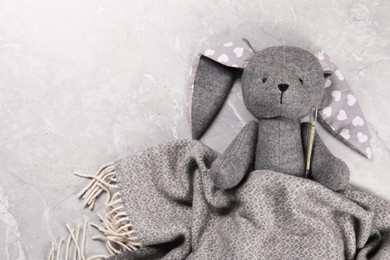 Toy bunny with thermometer under blanket on gray marble background, top view. Space for text