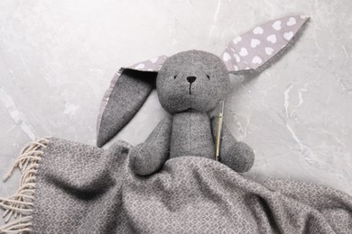 Photo of Toy bunny with thermometer under blanket on gray marble background, top view