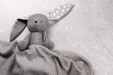 Toy bunny with thermometer under blanket on gray marble background, top view. Space for text