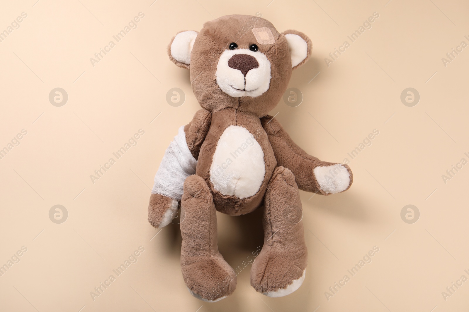 Photo of Toy bear with bandage on beige background, top view