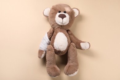 Toy bear with bandage on beige background, top view