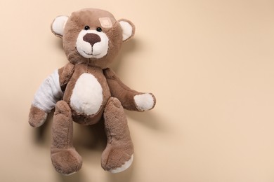 Photo of Toy bear with bandage on beige background, top view. Space for text