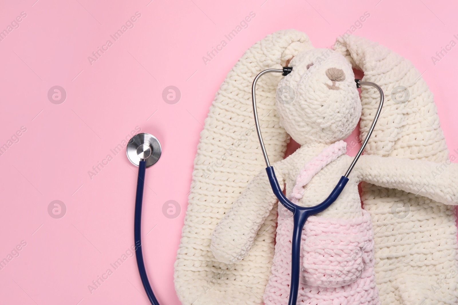 Photo of Toy bunny and stethoscope on pink background, top view. Space for text