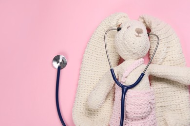 Toy bunny and stethoscope on pink background, top view. Space for text