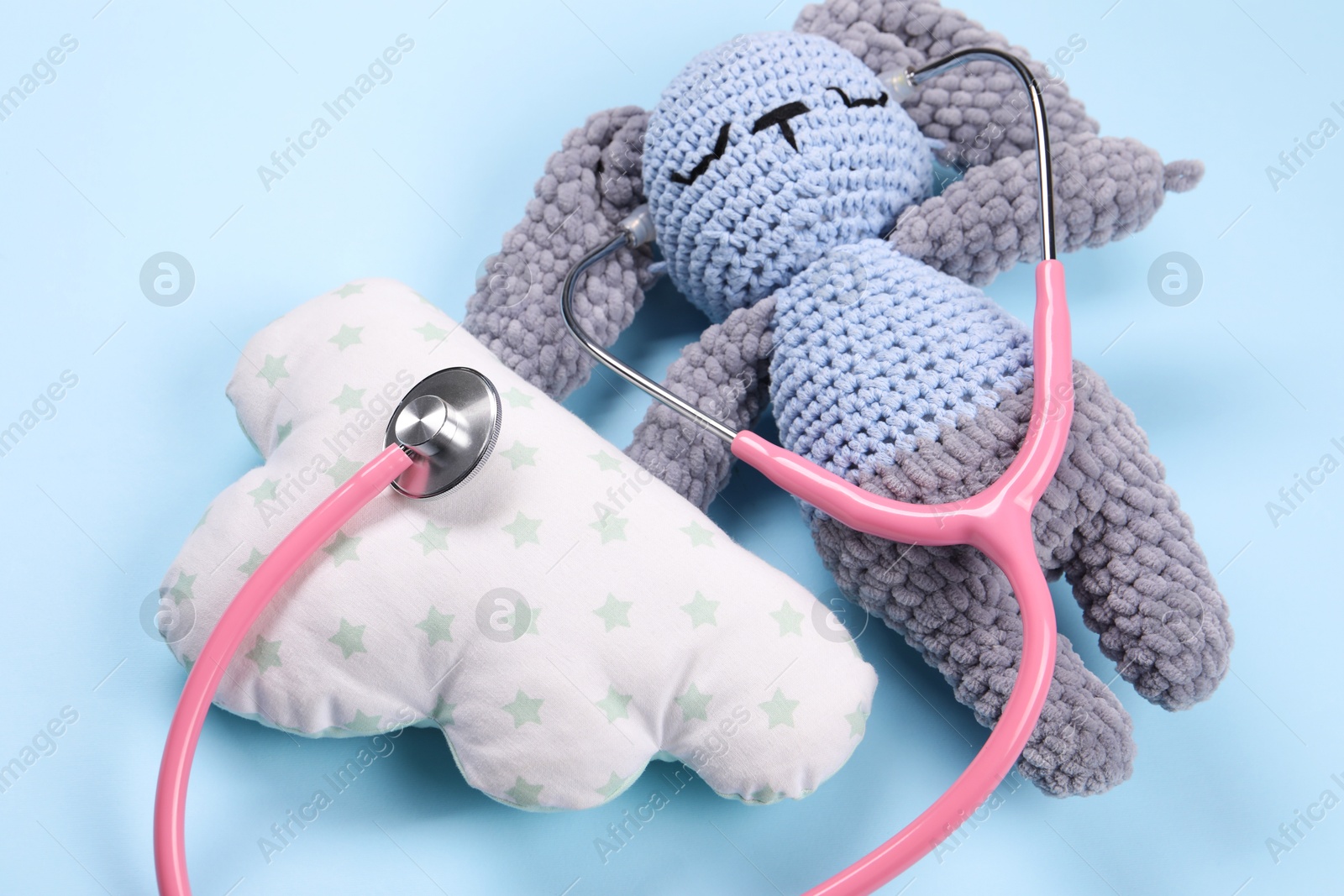 Photo of Toy bunny, pillow and stethoscope on light blue background, closeup