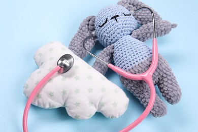 Toy bunny, pillow and stethoscope on light blue background, closeup