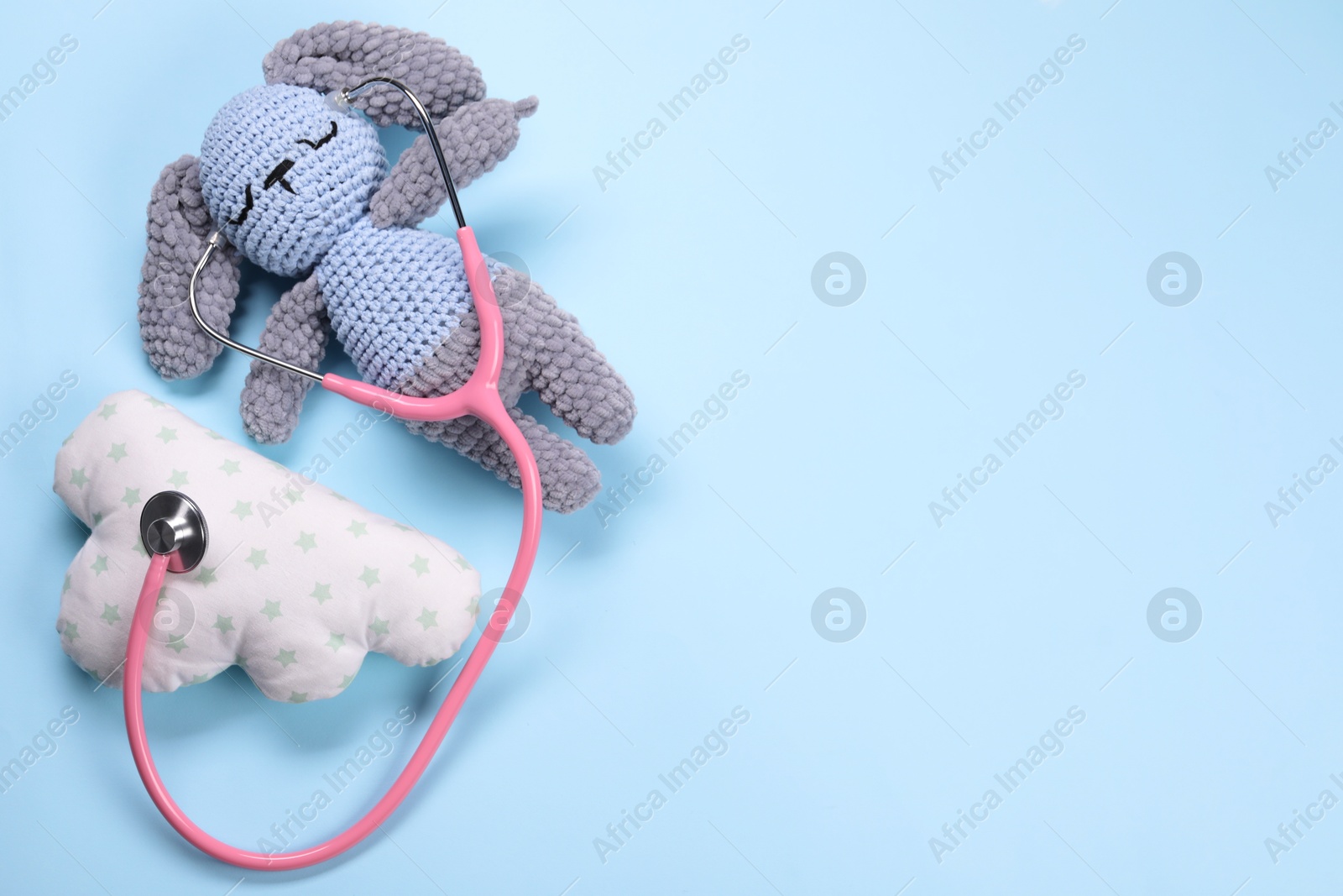 Photo of Toy bunny, pillow and stethoscope on light blue background, flat lay. Space for text