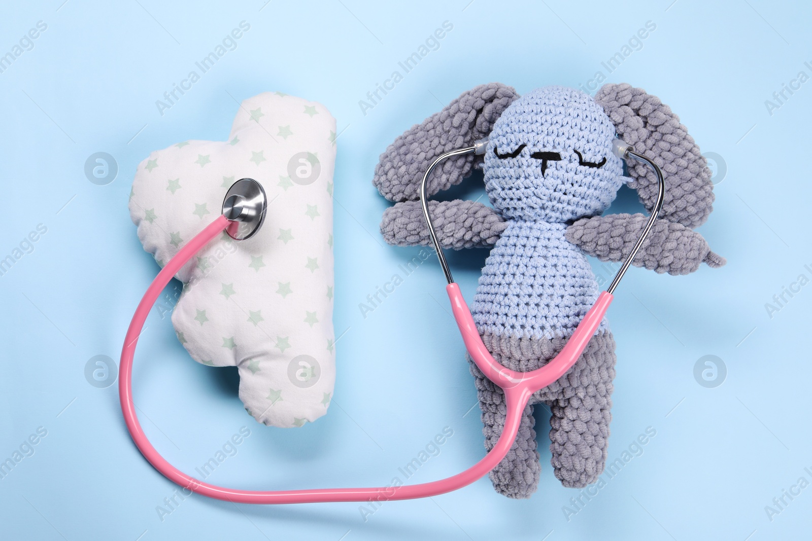 Photo of Toy bunny, pillow and stethoscope on light blue background, flat lay