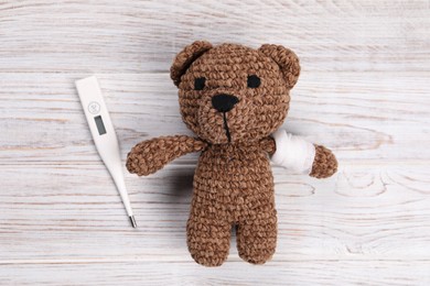 Toy bear and thermometer on wooden background, flat lay