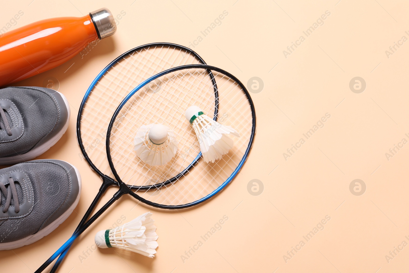 Photo of Feather badminton shuttlecocks, sneakers and bottle on beige background, flat lay. Space for text