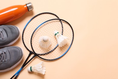 Feather badminton shuttlecocks, sneakers and bottle on beige background, flat lay. Space for text