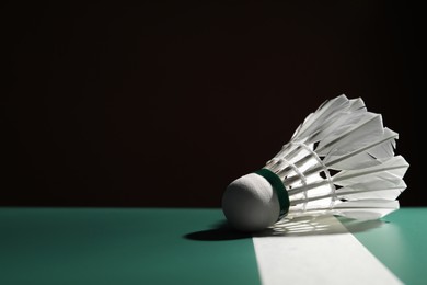 Feather badminton shuttlecock on green table against dark background, space for text