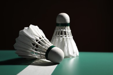 Photo of Feather badminton shuttlecocks on green table against dark background, space for text