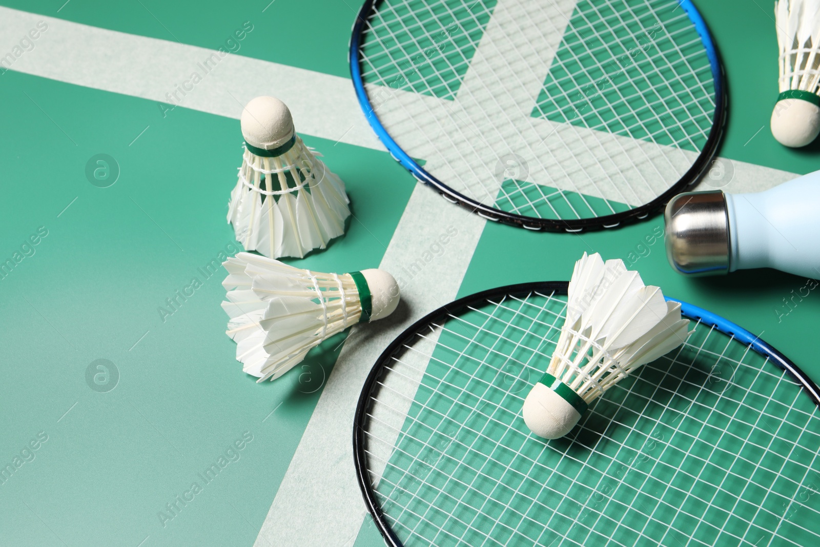 Photo of Feather badminton shuttlecocks, rackets and bottle on court