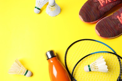 Photo of Feather badminton shuttlecocks, rackets, sneakers and bottle on yellow background, flat lay. Space for text