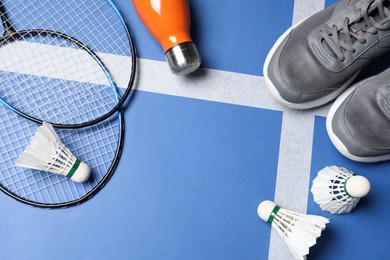 Feather badminton shuttlecocks, rackets, sneakers and bottle on court, flat lay. Space for text