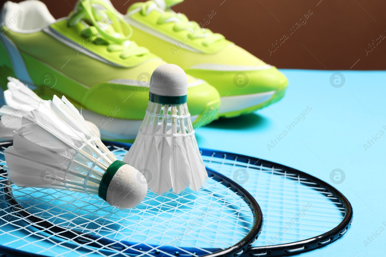 Photo of Feather badminton shuttlecocks, rackets and sneakers on light blue background, closeup