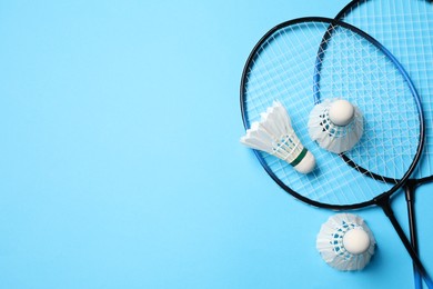 Photo of Feather badminton shuttlecocks and rackets on light blue background, flat lay. Space for text