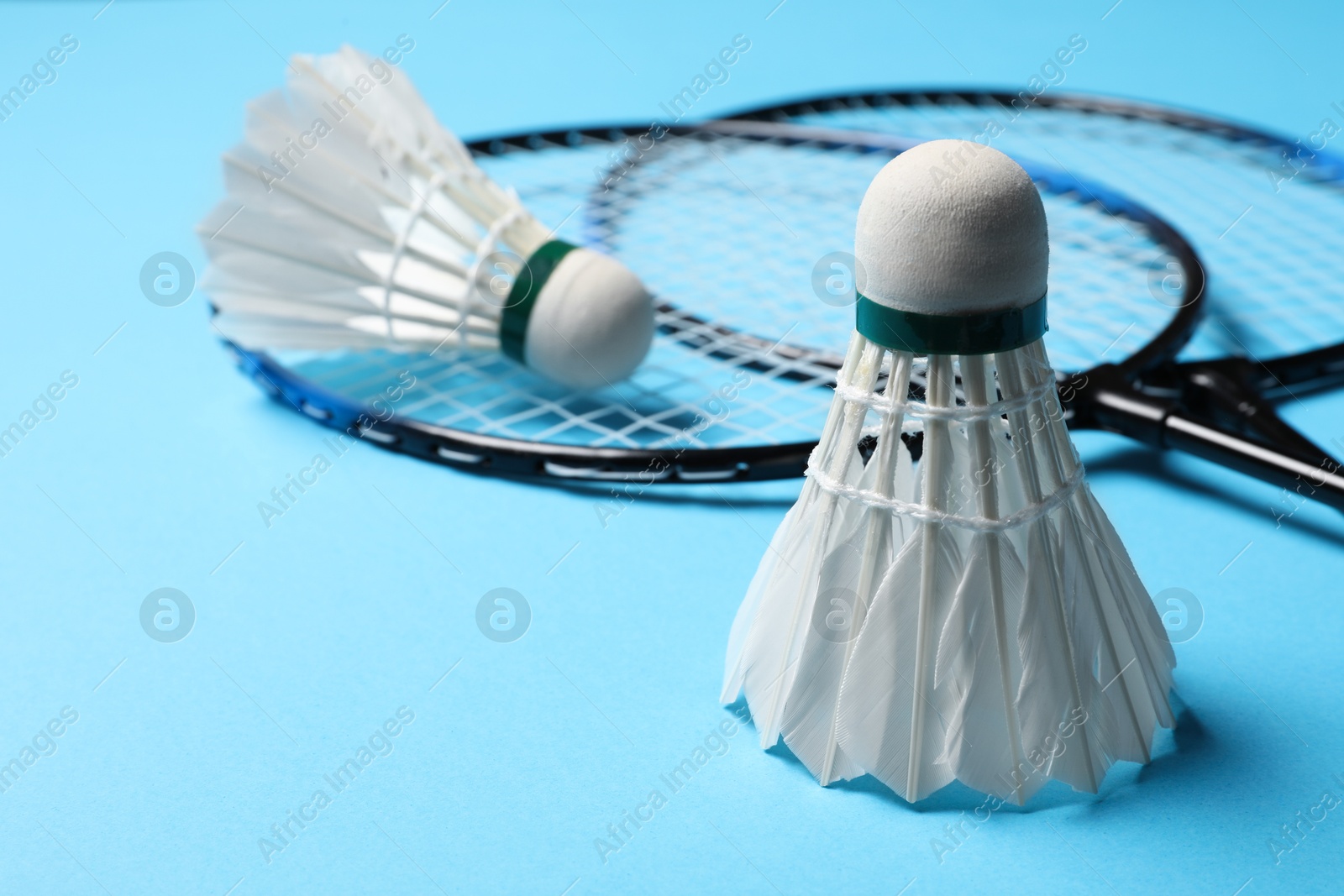 Photo of Feather badminton shuttlecocks and rackets on light blue background, closeup