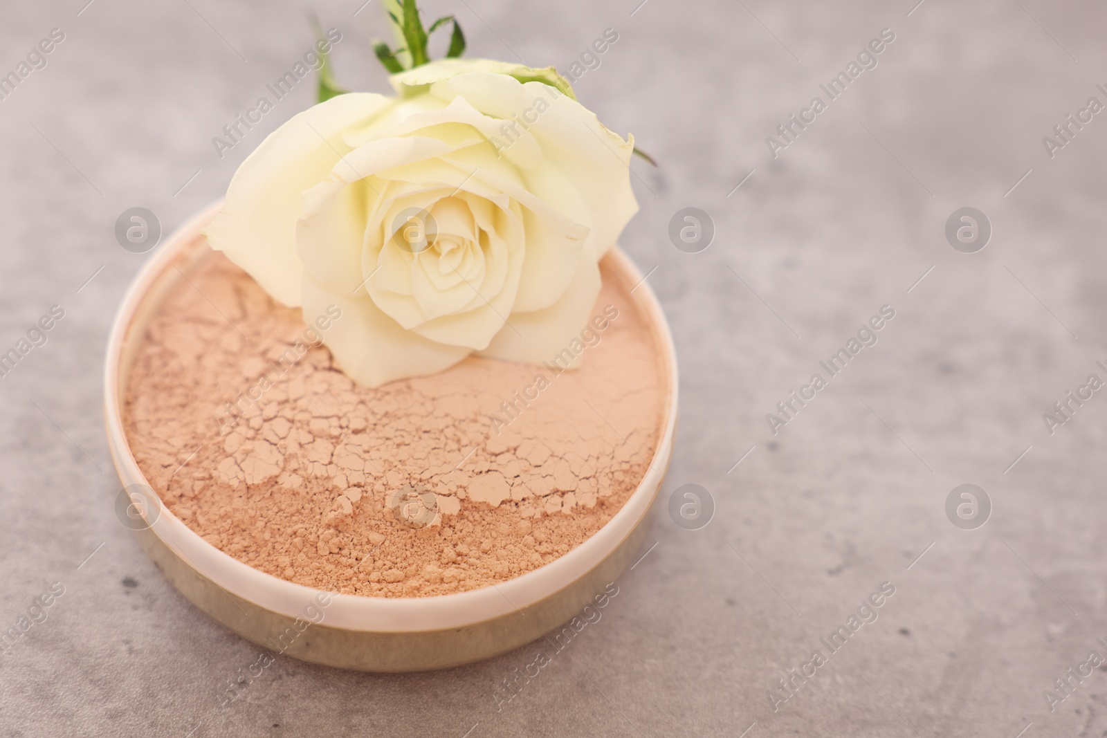 Photo of Face powder and rose flower on grey textured table, closeup. Space for text