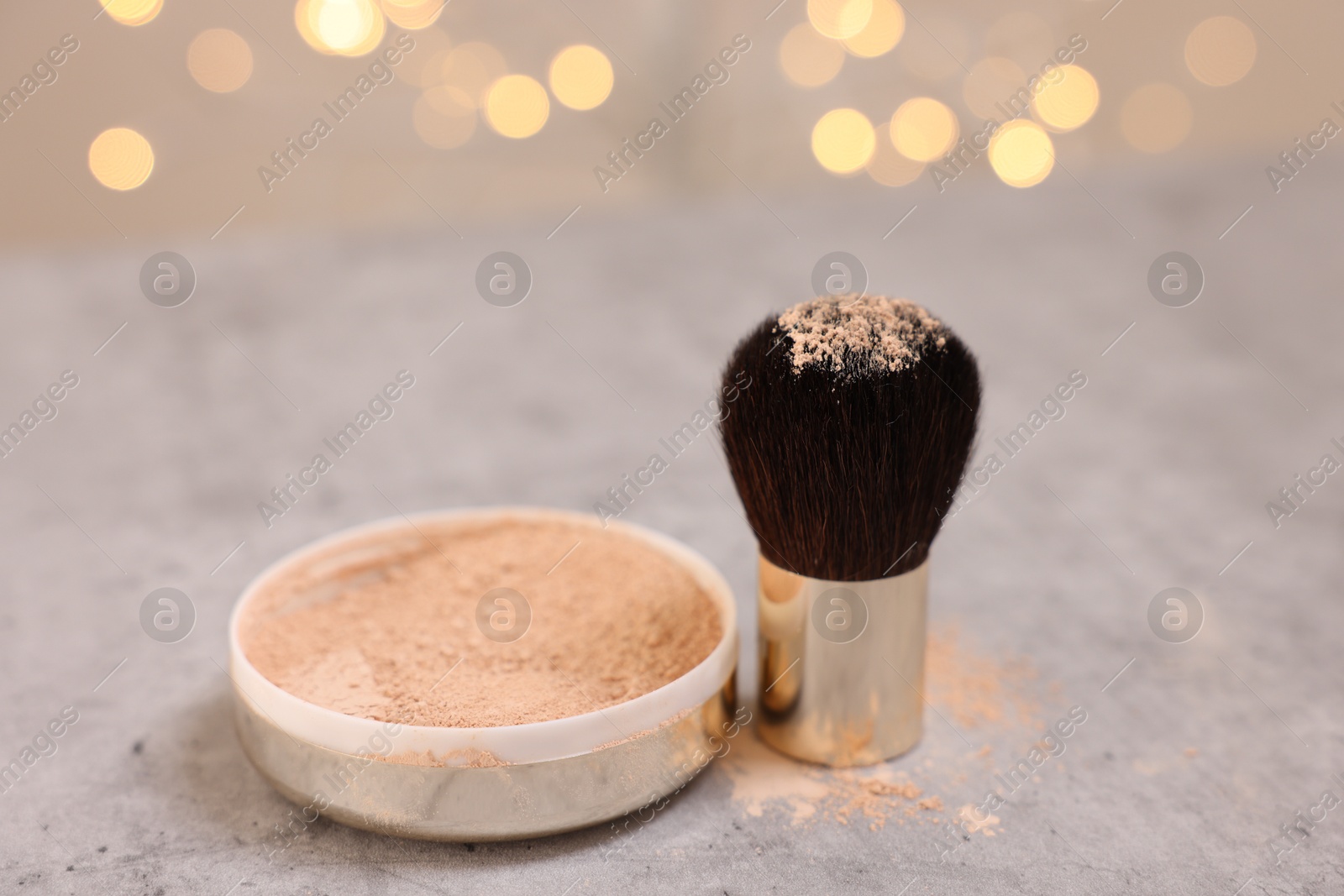 Photo of Face powder and brush on grey textured table against blurred lights, closeup