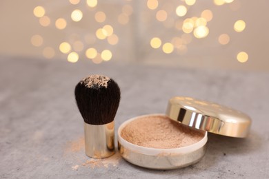 Photo of Face powder and brush on grey textured table against blurred lights, closeup