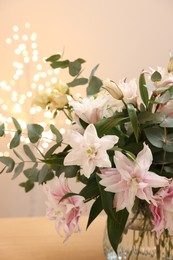 Photo of Bouquet of beautiful lily flowers in vase on table against beige background with blurred lights, closeup