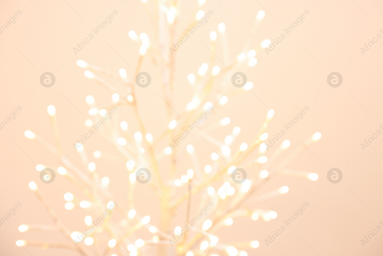 Photo of Decorative tree with lights on beige background, blurred view