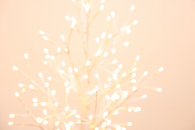 Photo of Decorative tree with lights on beige background, blurred view