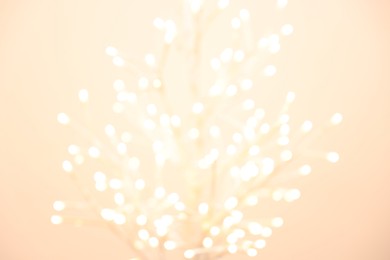 Photo of Decorative tree with lights on beige background, blurred view