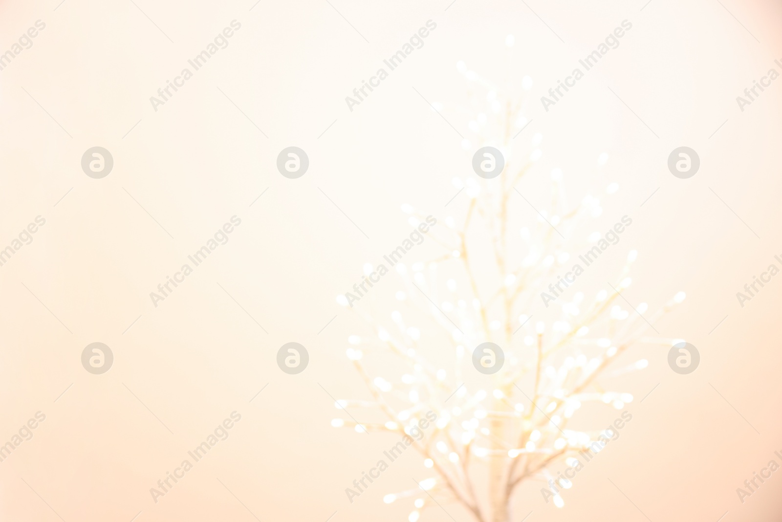 Photo of Decorative tree with lights on beige background, blurred view. Space for text